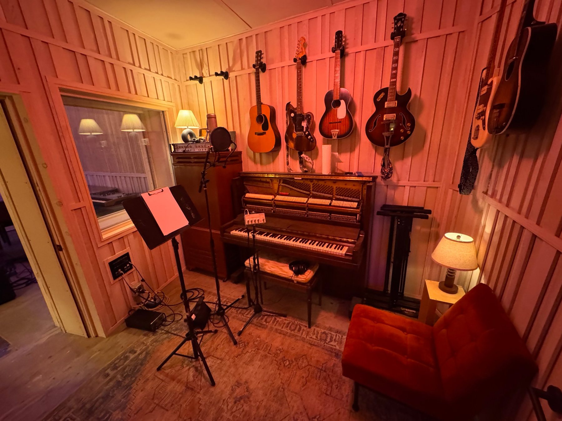 Booth with upright piano, hanging guitars and a vocal mic