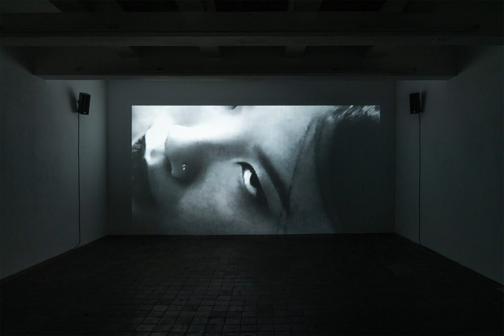 Cast Off installation view: a large black-and-white projection of a face in a dark gallery
